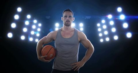 Male basketball player holding ball under arena lights showing strength and determination