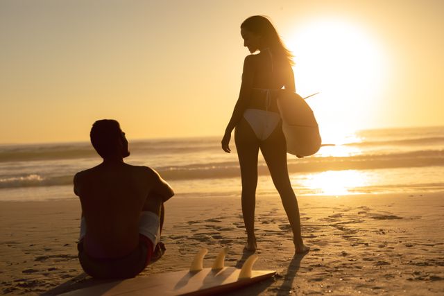 Couple enjoying a romantic moment on the beach during sunset, with surfboards in the foreground. Ideal for travel, vacation, romance, and lifestyle themes. Perfect for promoting beach destinations, summer activities, and outdoor adventures.