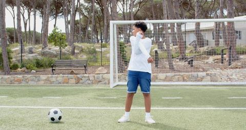 Boy stretching arms outdoors with soccer ball nearby