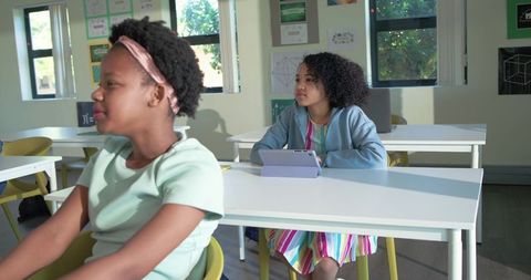 African american teen girls using tablet in bright classroom engaged in learning