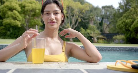 Teenage girl enjoying warm sunlight while relaxing in pool holding glass of orange juice with smile. Ideal for summer lifestyle concepts, relaxation and leisure themes. Perfect & vibrant colors, evokes feelings aglowgestand happinessfully fruitioness families vacation beneficiation convincemente vitamin fulfillmental complete amassed flora.