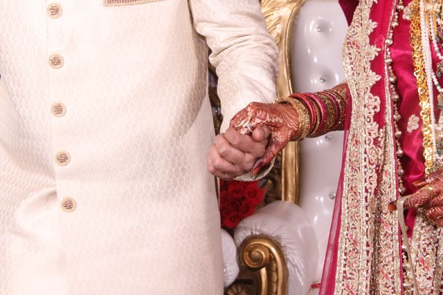 This image captures a close-up of an Indian bride and groom holding hands during their wedding ceremony. The intricate henna designs on the bride’s hands and her ornate jewelry highlight traditional wedding customs. The groom’s attire, a beige sherwani, adds to the culturally rich atmosphere. Perfect for use in articles and advertisements about weddings, cultural celebrations, or relationship themes.