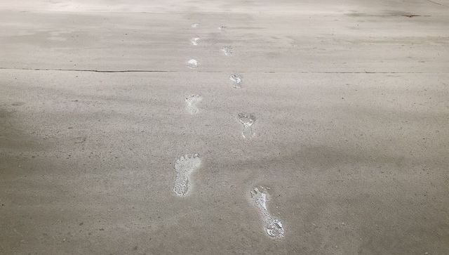 Barefoot footprints leading across damp concrete slab receding into distance minimal trail