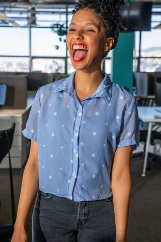 Joyful african american woman laughing in modern office wearing polka-dot blouse