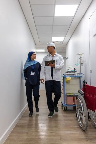 Clinical team walking hospital corridor consulting tablet discussing patient care teamwork