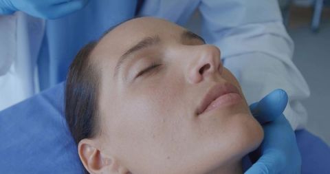 Doctor supporting female patient jaw with blue gloves during facial examination, reclining