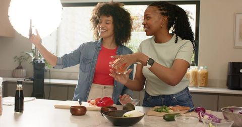 Diverse female friends prepping salmon and filming cooking video at home kitchen island