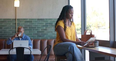 Woman reading paperback at sunlit cafe counter, remote worker enjoying morning coffee