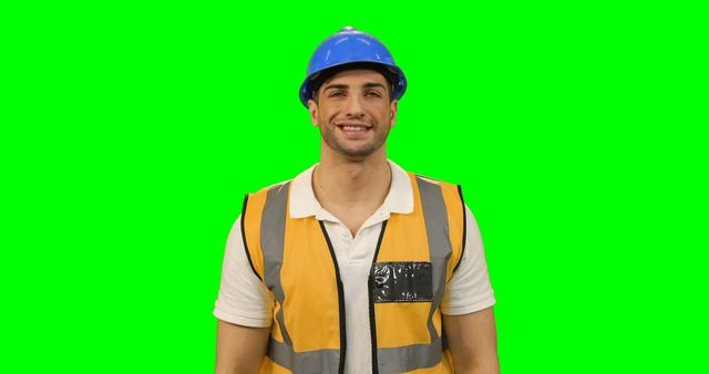 Smiling construction worker wearing hi-vis vest and blue hard hat stands against green screen background. Ideal for themes related to occupational safety, construction, industrial workforce, promotional materials, safety training programs, or realistic job simulations.