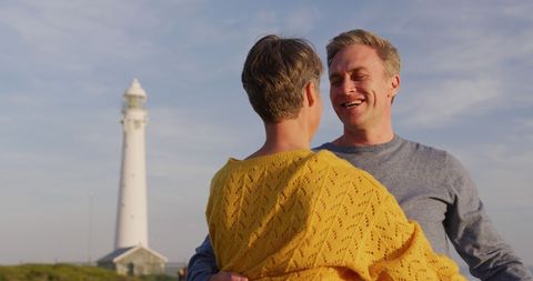 Senior Couple Embracing Near Lighthouse at Sunset