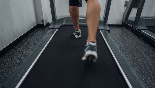 Close-up running legs on treadmill wearing black shorts and running shoes for cardio workout