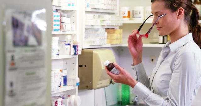 The pharmacist is examining a prescription bottle, suggesting careful attention to medication details. Ideal for content related to healthcare, medication management, pharmacy operations, pharmaceutical industry, healthcare professionals, and patient care.