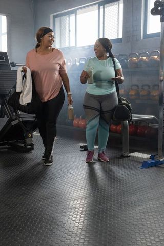 Plus-size african american women walking and laughing in gym carrying shaker bottles
