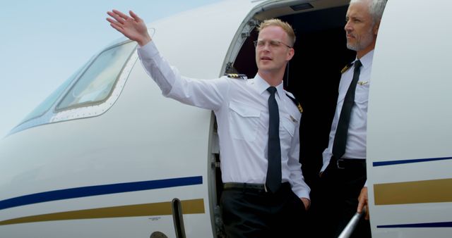 Two commercial airline pilots in uniform stand at the door of an airplane on the tarmac. One pilot points and discusses something, while the other listens attentively. This image could be used for airline advertising, aviation stories, or illustrating workplace professionalism among pilots.