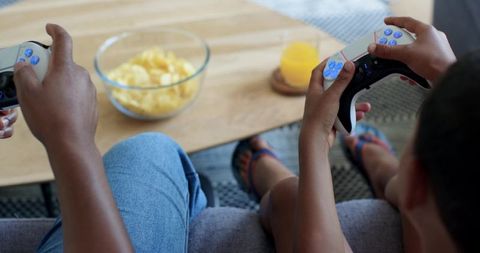 African american father and son playing video games on couch with controllers and snacks