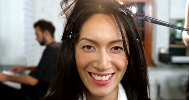 A smiling Asian woman is getting her hair styled at a salon, with copy space. Her cheerful expression suggests a pleasant and satisfying experience during her beauty routine.