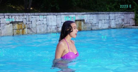 Woman speaking while wading in sunlit pool wearing magenta bikini top rippling reflections
