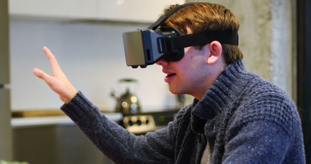 Young man wearing a VR headset in a modern home. Engaged in interactive, immersive virtual reality gaming. Can be used in technology promotion, gaming ads, or educational VR experiences.