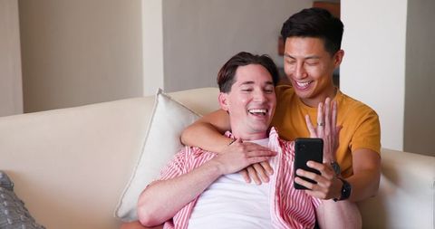 Diverse Gay Couple Smiling on Couch While Using Smartphone