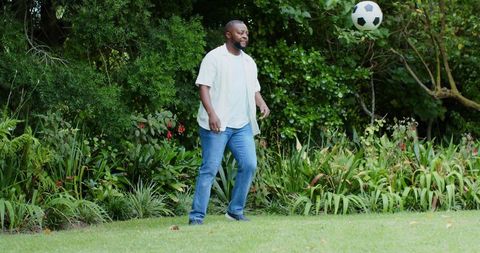 African american man kicking soccer ball on backyard lawn surrounded by lush garden