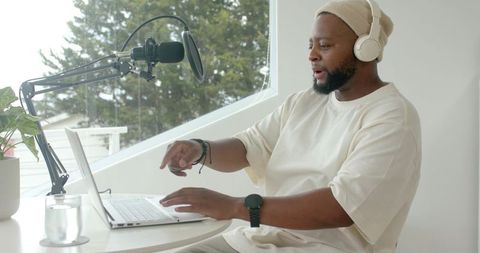 African male recording podcast in minimalist studio with laptop, microphone, headphones
