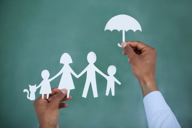 Man protecting paper cut out family with umbrella on green background