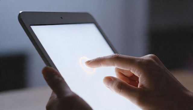 Tapping tablet touchscreen with orange indicator, two-hand hold, minimal tech workspace
