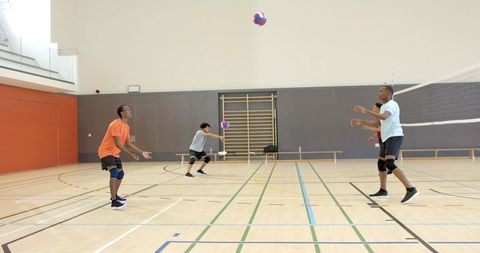 Multiracial male teammates practicing two-ball volleyball drill on indoor wooden court