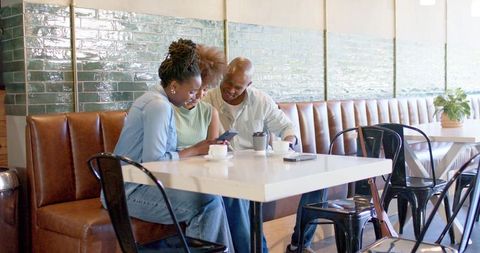 African american friends leaning in sharing smartphone at cafe table with coffee cups