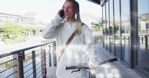 Man talking on phone while walking bicycle along urban waterfront with digital binary overlay
