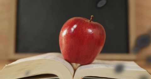 Fresh red apple on open book in classroom setting