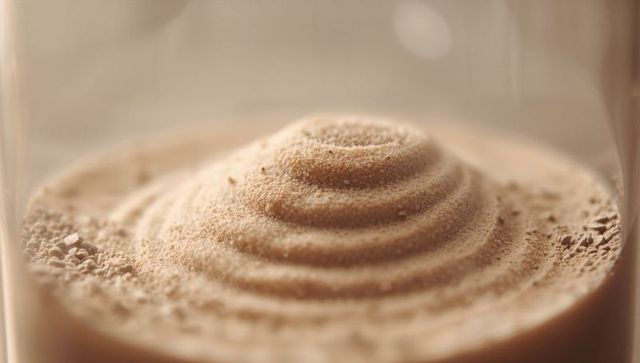 Abstract concentric mound of beige sand inside glass vessel