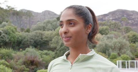Serene Indian woman standing outdoors on hillside wearing green zip-up top