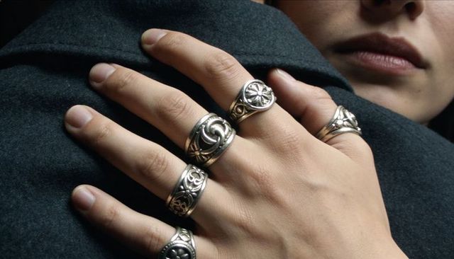 Close-up hand resting on shoulder wearing ornate silver rings on dark wool coat