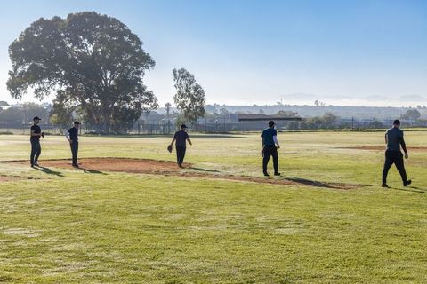 Five teammates standing on baseball field at sunrise casting long shadows early morning teamwork