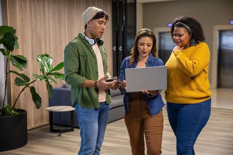 Diverse coworkers collaborating over laptop and phone in modern office lounge
