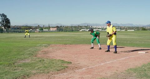 Men Playing Baseball Near First Base Wearing Yellow and Green Uniforms on Sunny Field