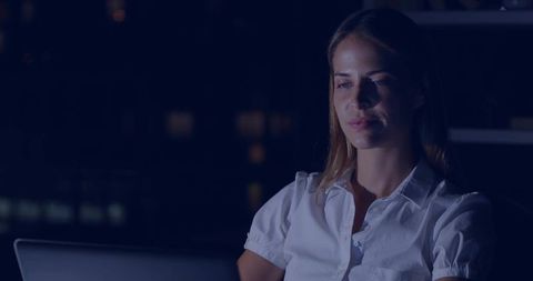 Mid-adult woman working late on laptop with blue screen glow, focused remote work at night