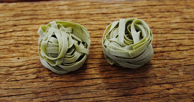 Close-up detail of green pasta nests placed on rustic wooden surface. Ideal for use in culinary articles, recipe websites, or food-related advertisements to emphasize organic and homemade cooking. Excellent for showcasing ingredients in healthy eating contexts and Italian cuisine promotions.