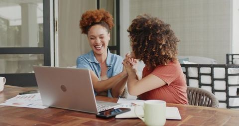Friends laughing and celebrating while collaborating on laptop with charts in sunroom