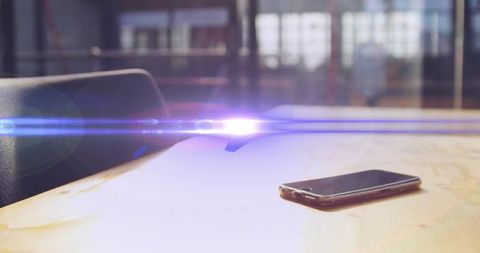 Minimal smartphone resting on worn wood desk with dramatic lens flare and window light