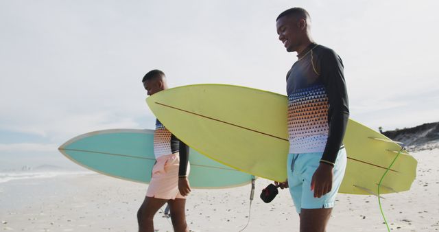 Two young surfers walking along the beach with their surfboards in the morning, near the ocean. This image is perfect for promoting beach vacations, surf gear, athletic lifestyles, youth culture, summer activities, or bonding experiences between friends.