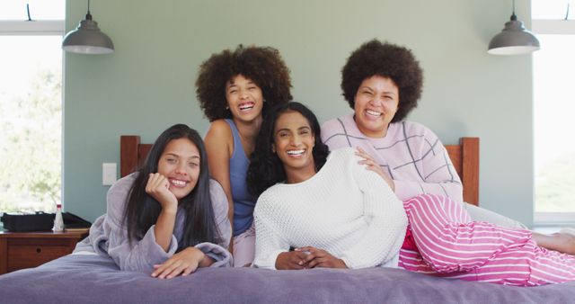 Portrait of happy diverse female friends lying on bed and smiling in bedroom. spending quality time at home.