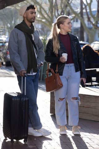 Sunlit urban couple walking with suitcase and coffee, casual travel and city lifestyle