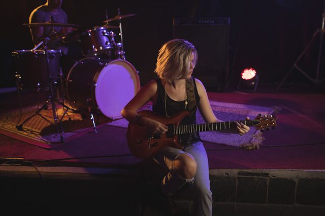 Female guitarist practicing on stage in a dimly lit nightclub, creating a moody and artistic atmosphere. Ideal for use in music-related content, concert promotions, band posters, and articles about live performances and nightlife.
