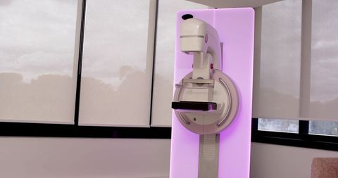 Mammography machine featuring purple backlit panel and clear compression paddle for breast screening