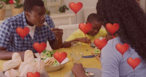 family gathered at table enjoying meal underscored by floating heart-shaped balloons creating celebratory ambiance. perfect for illustrating themes of love, family time, festive gatherings, and homey happiness in editorials and promotional content.