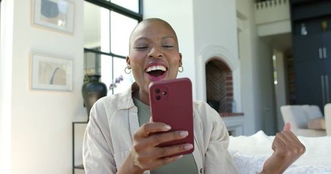 African american woman celebrating big win on smartphone in bright modern living room