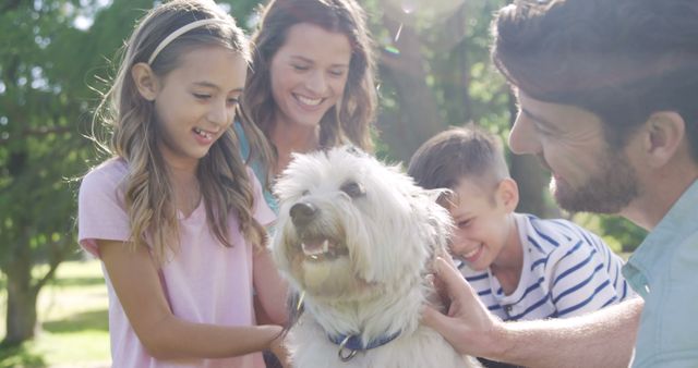 A Caucasian family enjoys a sunny day outdoors with their fluffy white dog, with copy space. Smiling faces and a shared moment with a pet reflect a warm, family bonding experience.