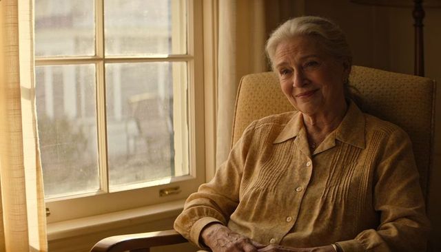 Serene senior woman sitting in armchair by sunlit paned window, warm cozy home portrait
